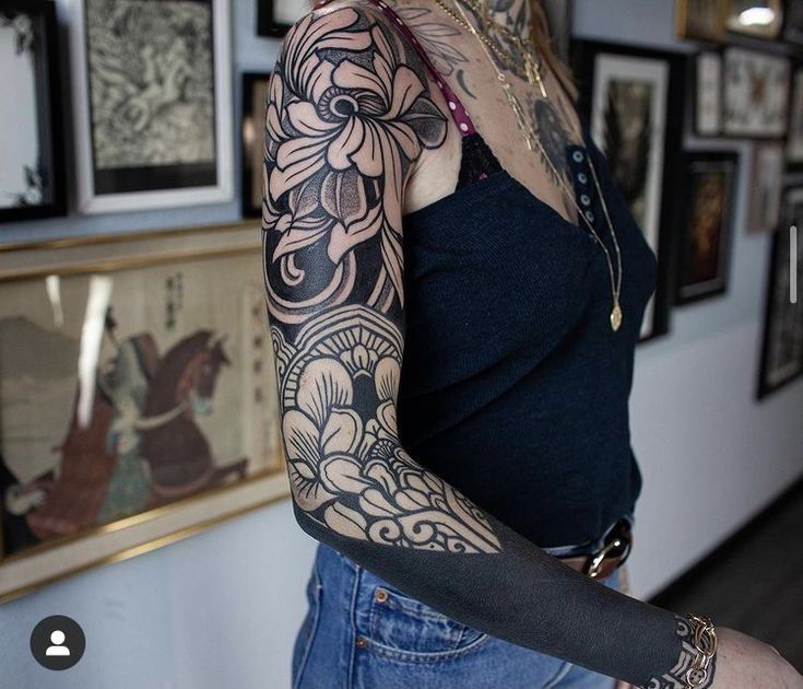 a woman with tattoos on her arms and arm is standing in front of a wall full of pictures