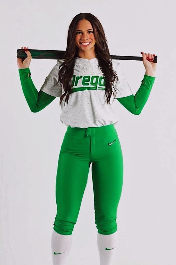 a woman in green pants holding a baseball bat over her head and smiling at the camera