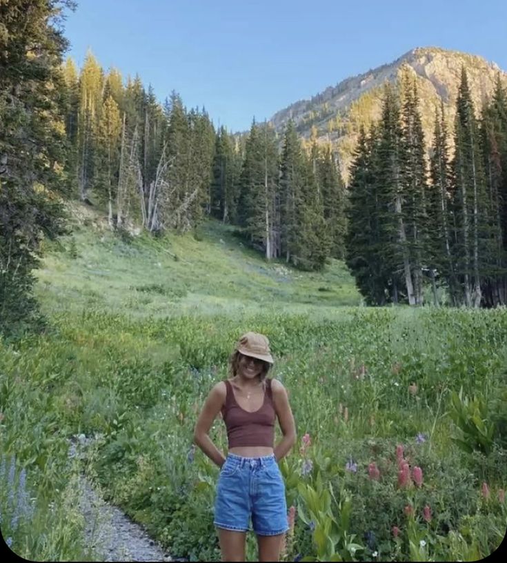 a woman standing in the middle of a field with mountains in the backgroud