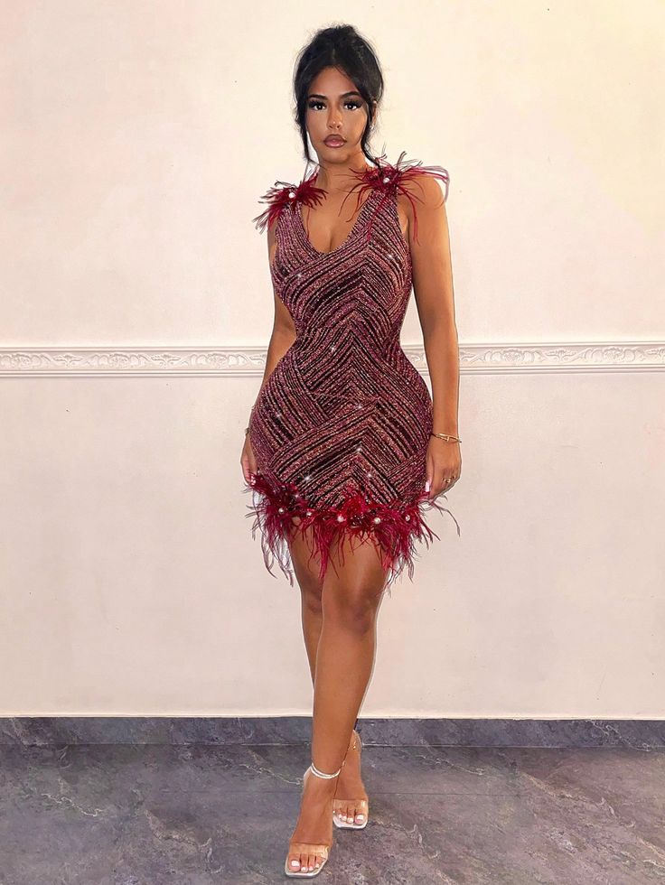 a woman in a short dress with feathers on the skirt and heels is standing against a wall