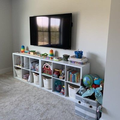 a television mounted on the wall in a living room with toy bins and toys