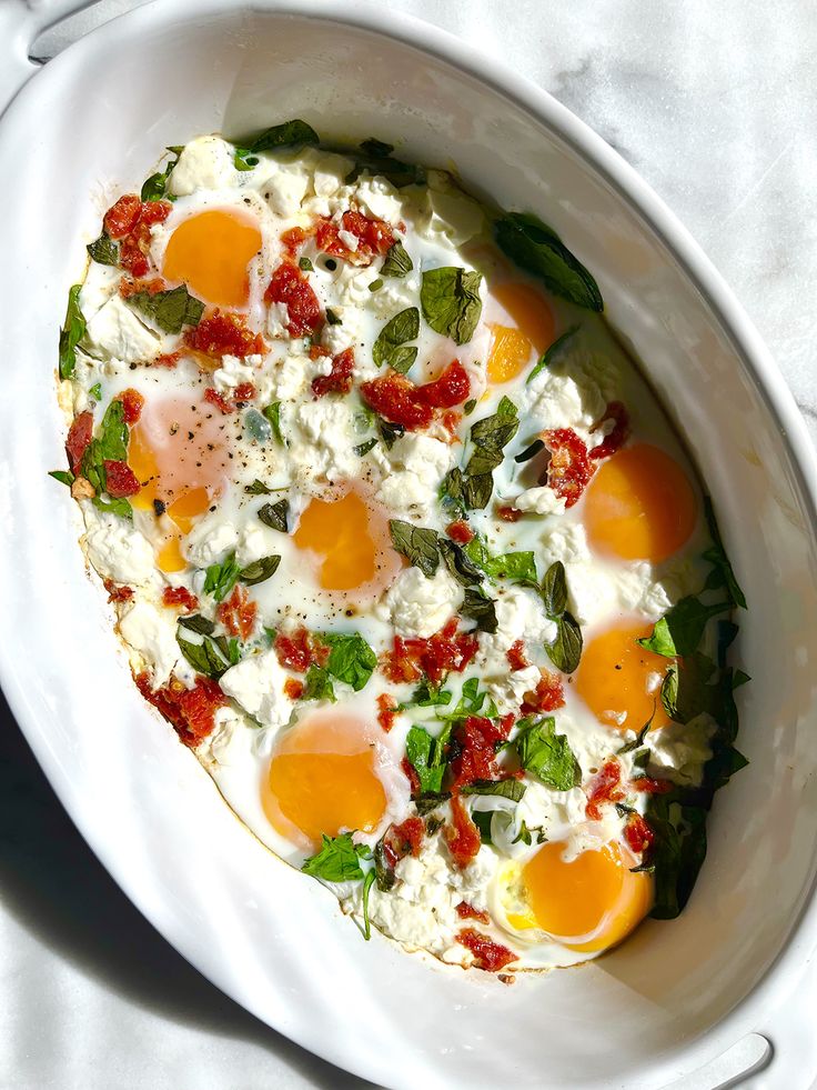 an egg dish with spinach and tomatoes in a white bowl on a marble surface