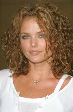 a close up of a woman with curly hair and blue eyes wearing a white shirt