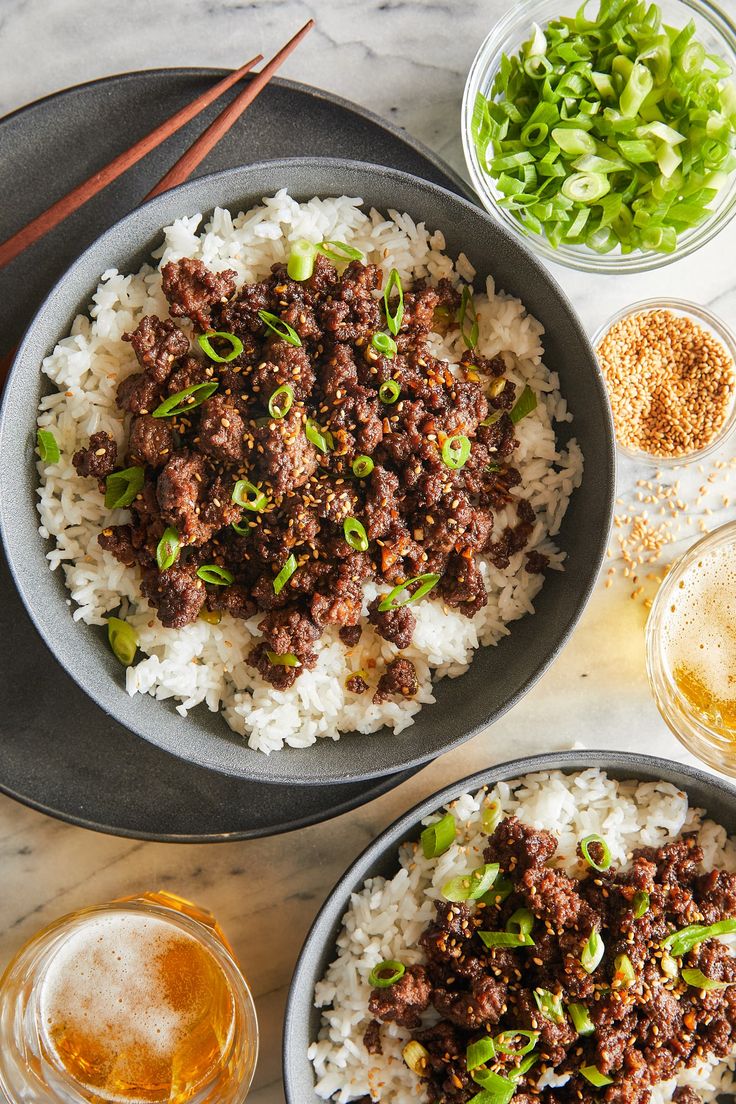 two bowls filled with meat and rice next to chopsticks on a marble table