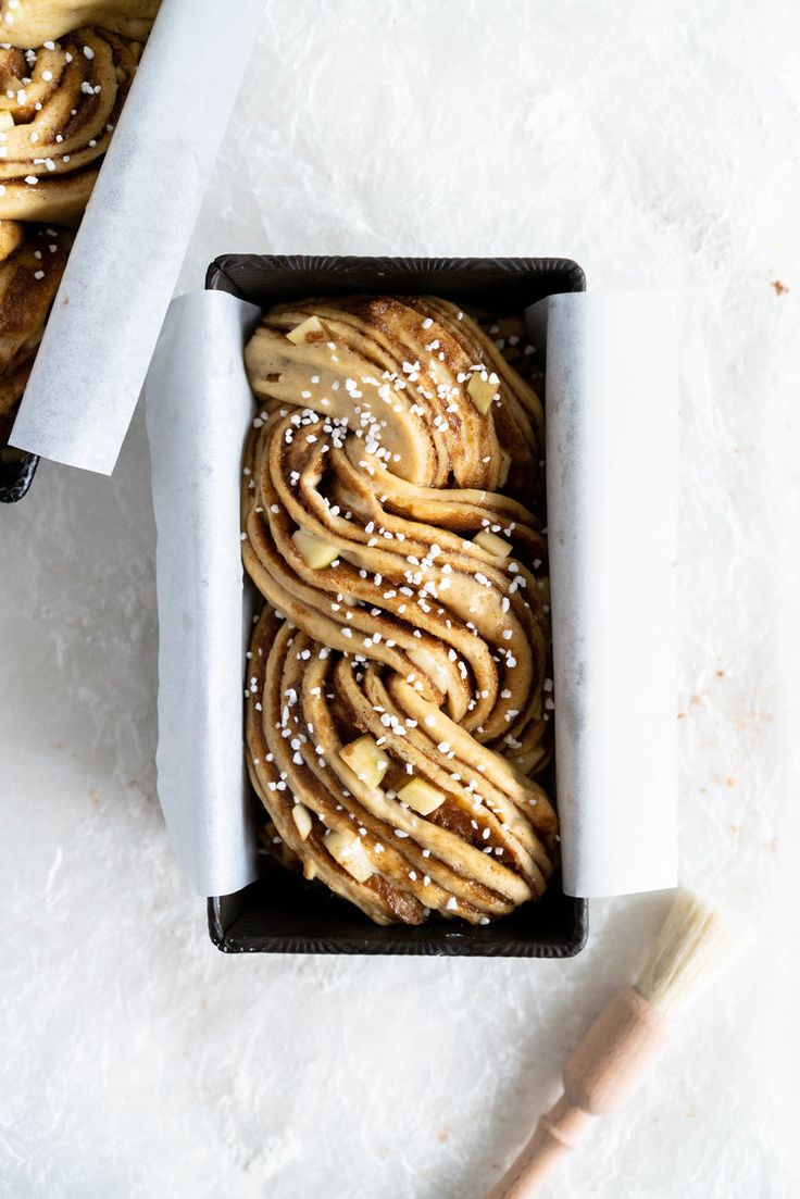 a box filled with cinnamon rolls on top of a white countertop next to a wooden spoon