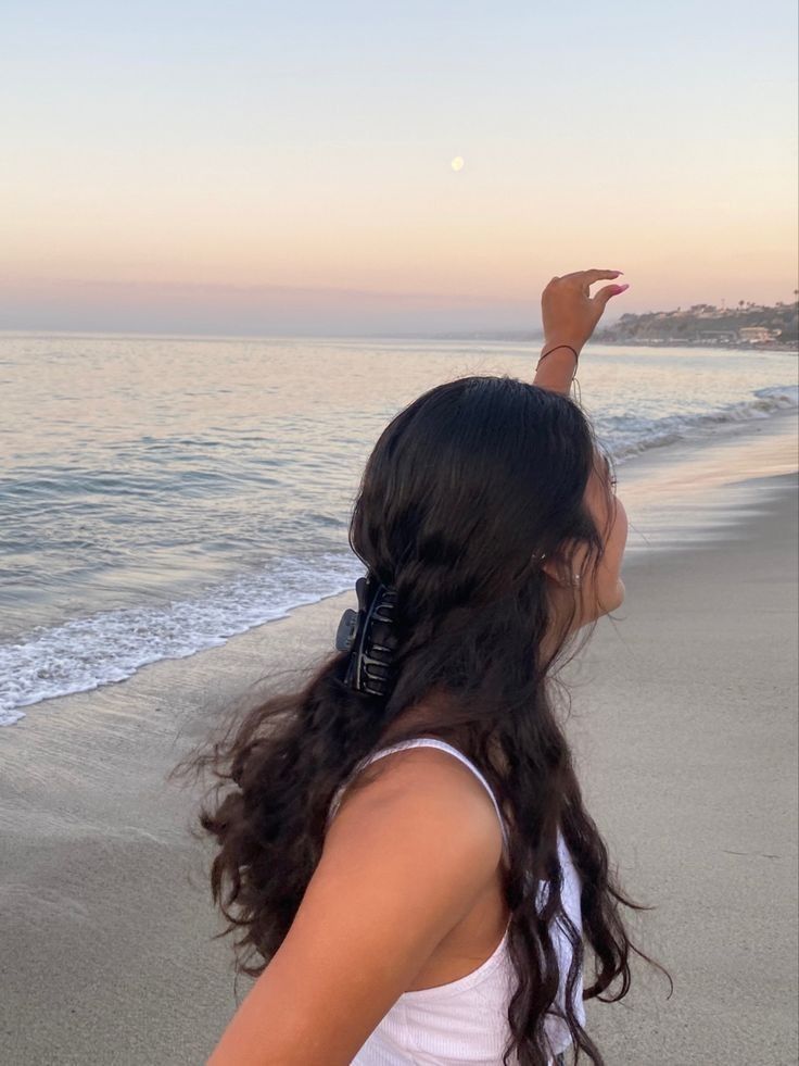 a woman standing on top of a beach next to the ocean holding her hand up