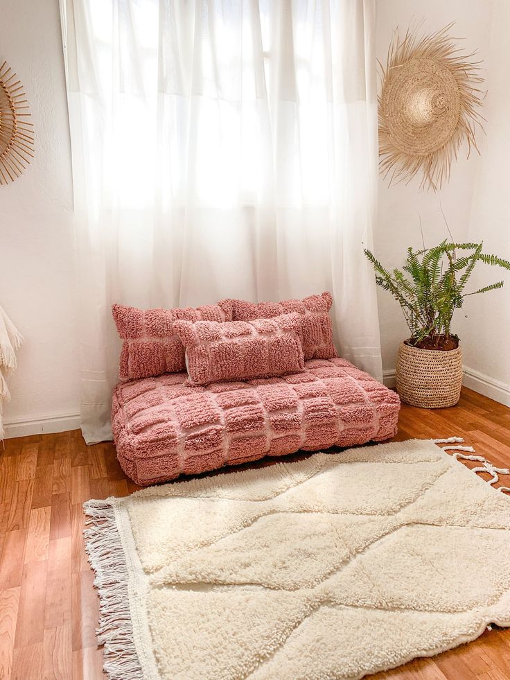 a pink couch sitting on top of a hard wood floor next to a potted plant