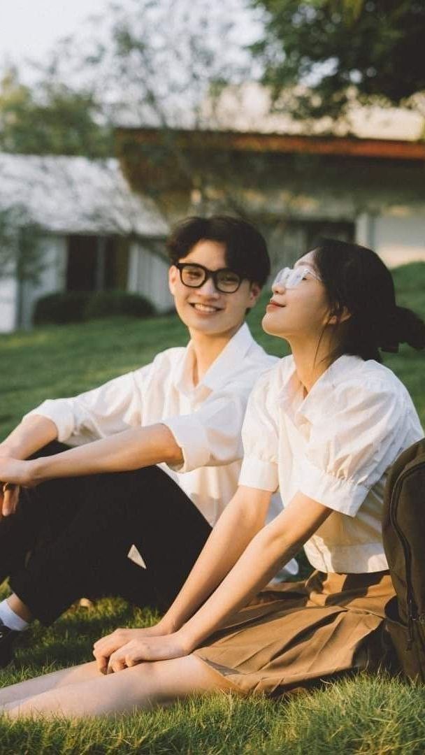 two people sitting on the grass in front of a house