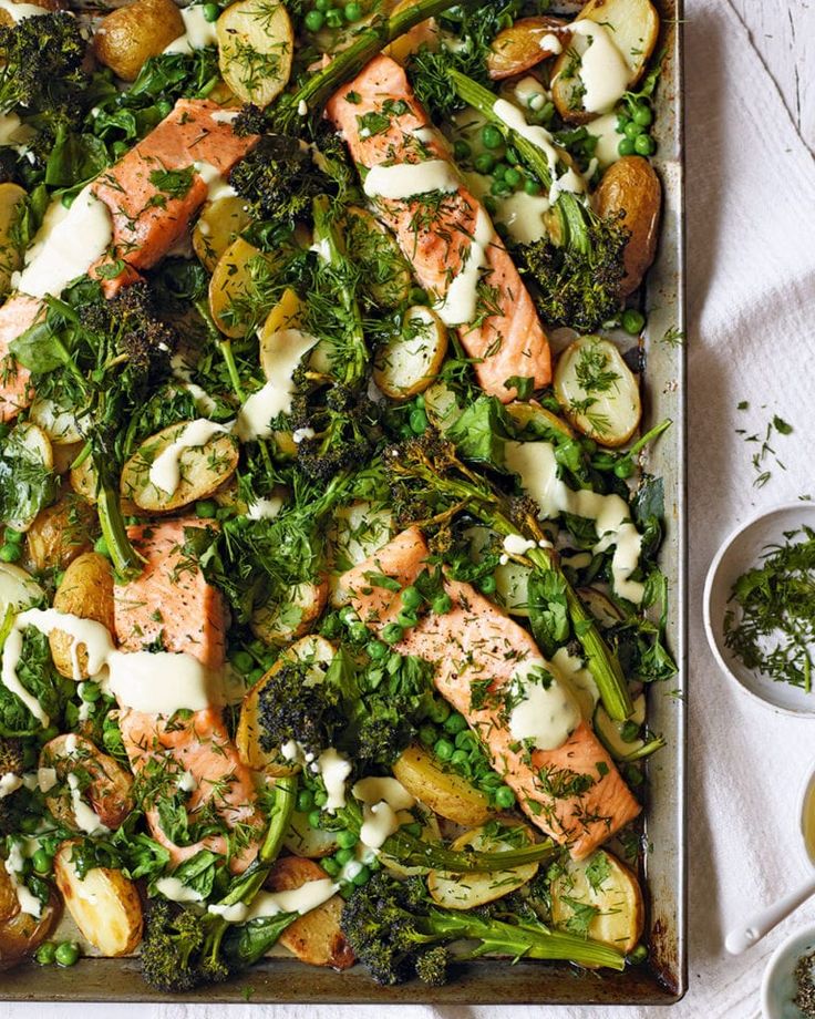 a sheet pan filled with salmon, broccoli and potatoes on top of a table