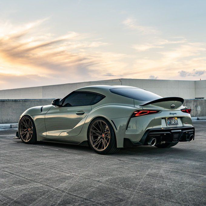 a grey sports car parked in a parking lot with the sun setting on it's roof