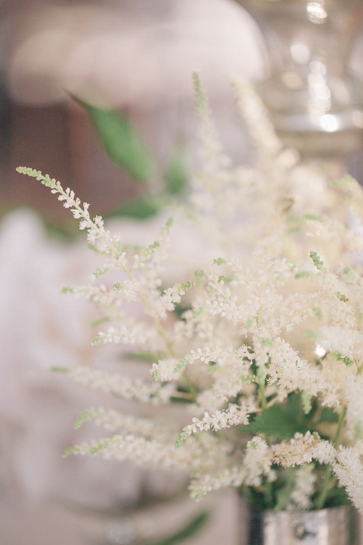 white flowers in a silver vase sitting on a table next to a candle holder with candles