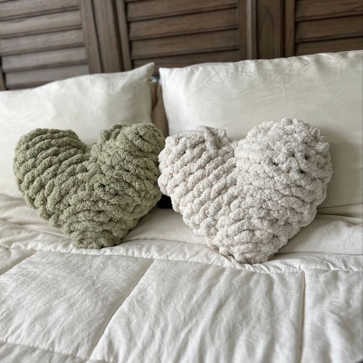 two knitted heart pillows sitting on top of a bed