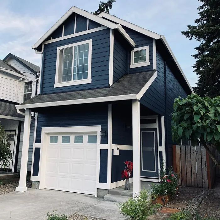 a two story house with blue siding and white garage doors on the front side of it