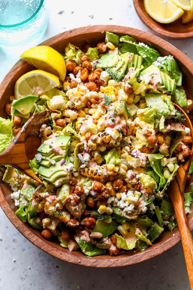 a wooden bowl filled with salad next to two lemon wedges