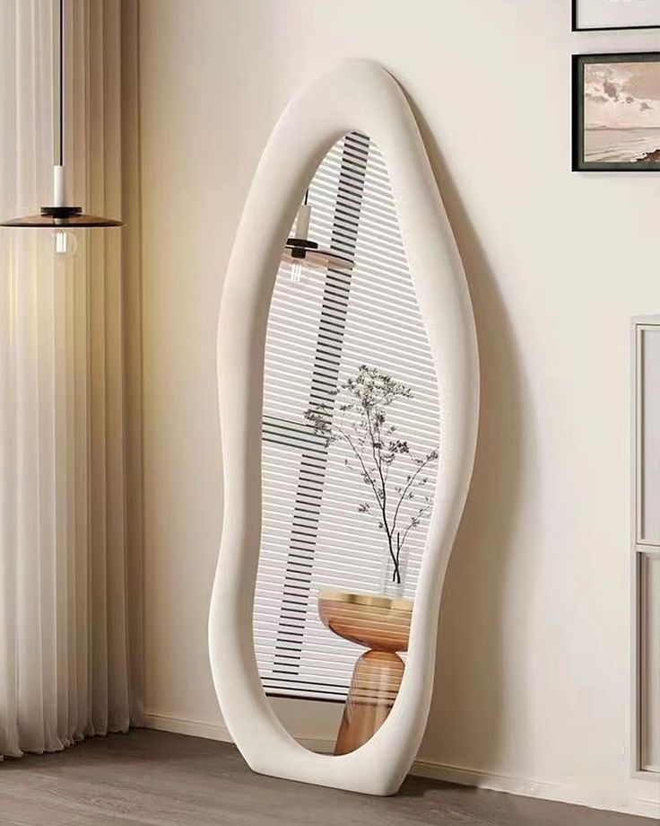 a large white mirror sitting on top of a wooden floor next to a vase with flowers in it