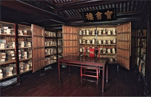 a room with shelves filled with lots of books and boxes on the wall next to a wooden table