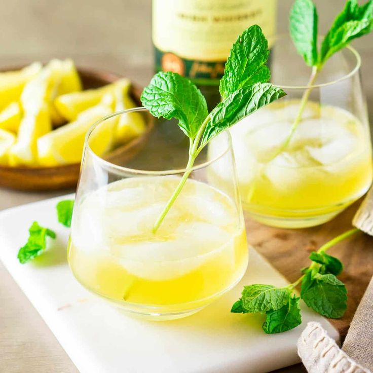 two glasses filled with lemonade and mint garnish on top of a cutting board