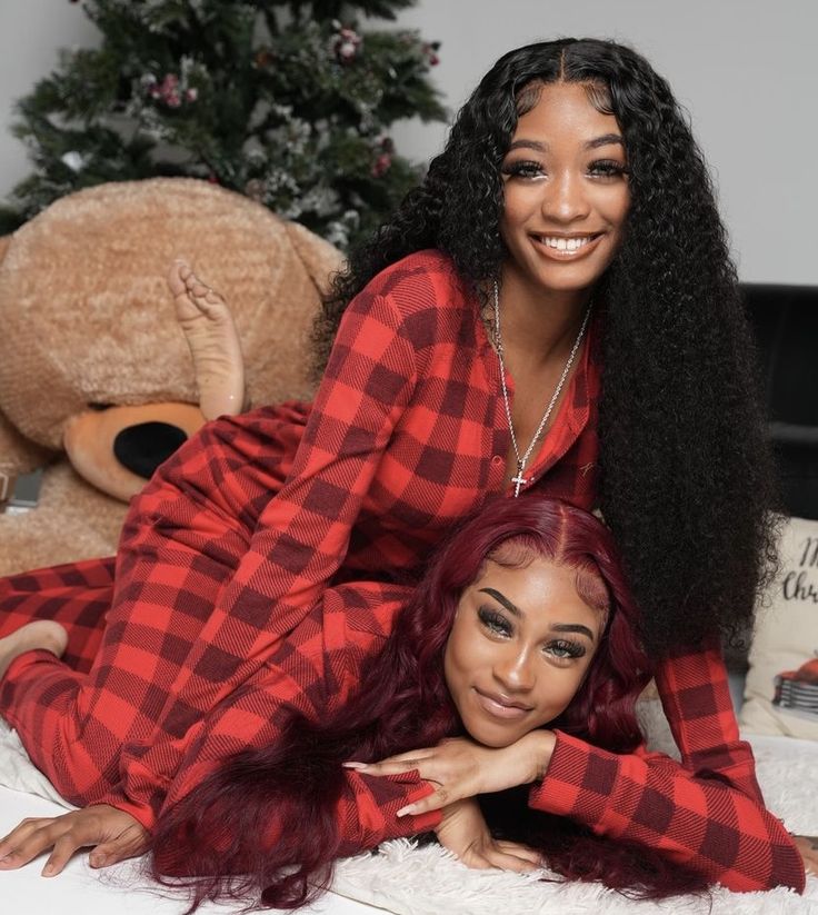 two women laying on a bed next to a teddy bear and christmas tree in the background