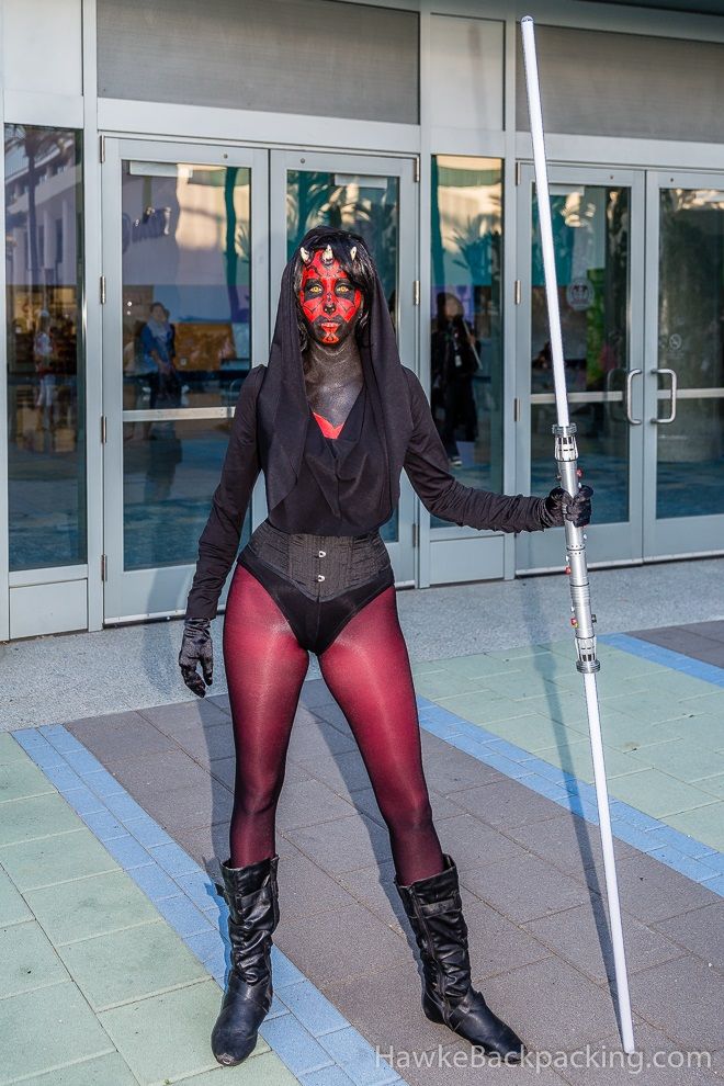 a woman dressed in black and red poses with a pole on the street while wearing her costume