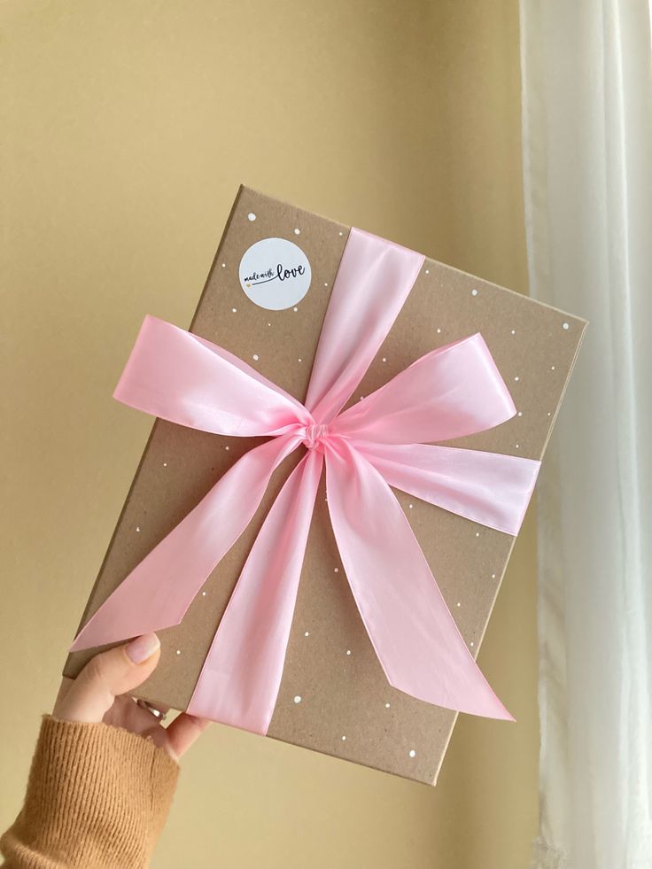 a person holding up a brown and pink gift box with a pink bow on it