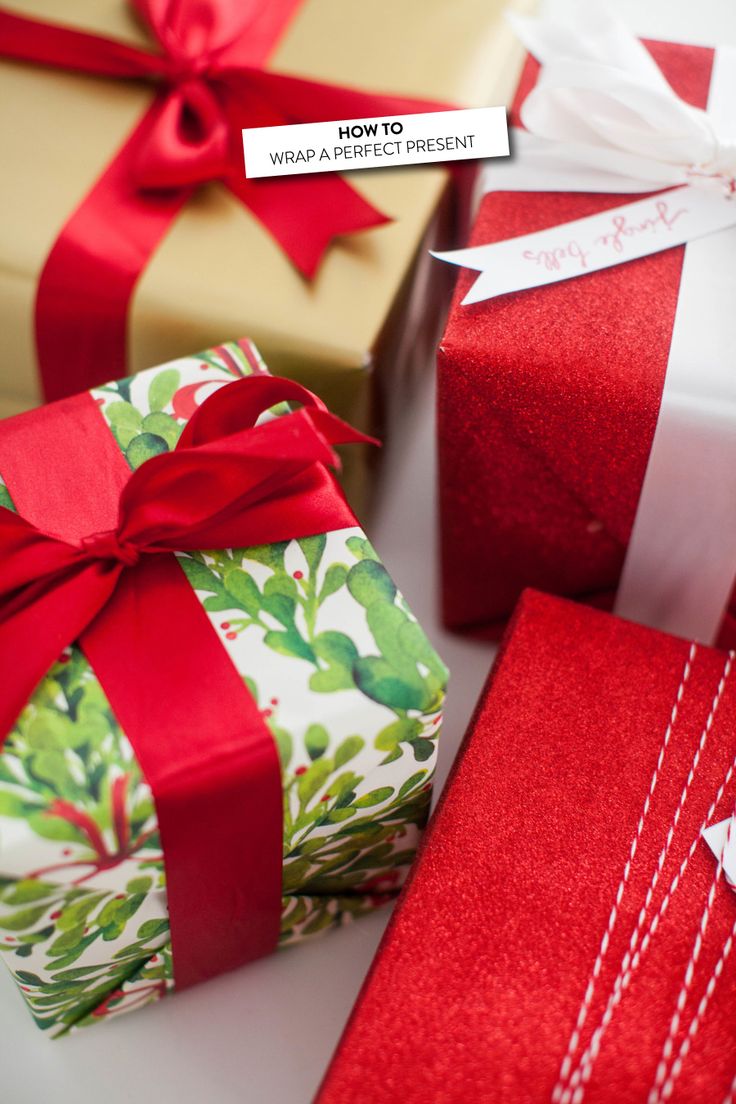 three wrapped presents sitting next to each other on top of a white table with red ribbon