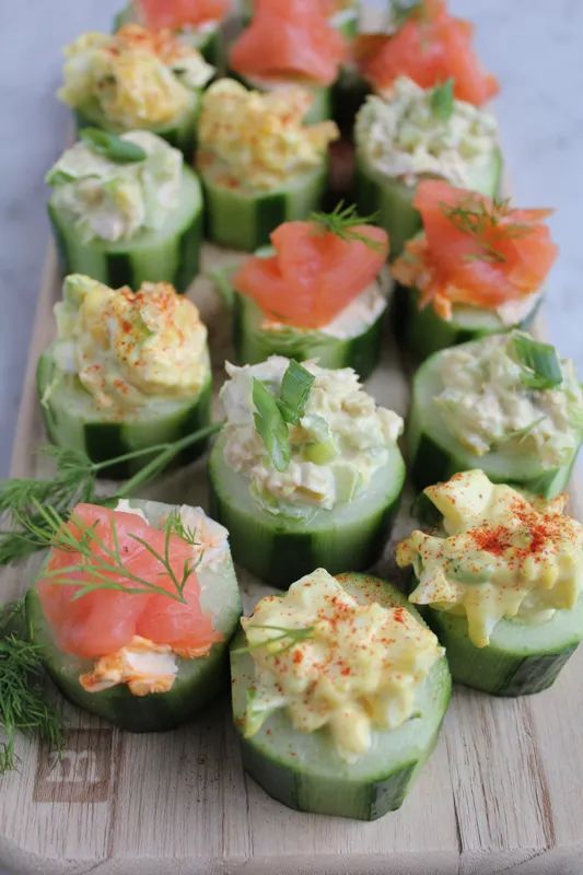 cucumbers stuffed with salmon and cream cheese are arranged on a cutting board to be served