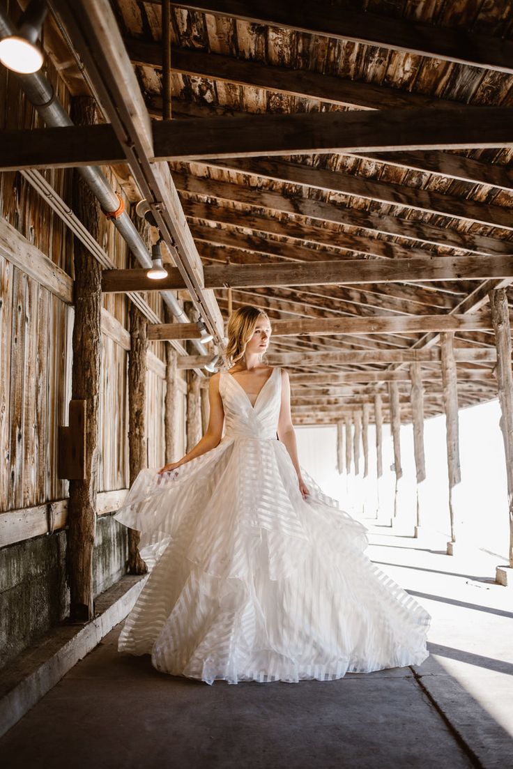 a woman in a white wedding dress is posing for the camera while standing under a wooden structure