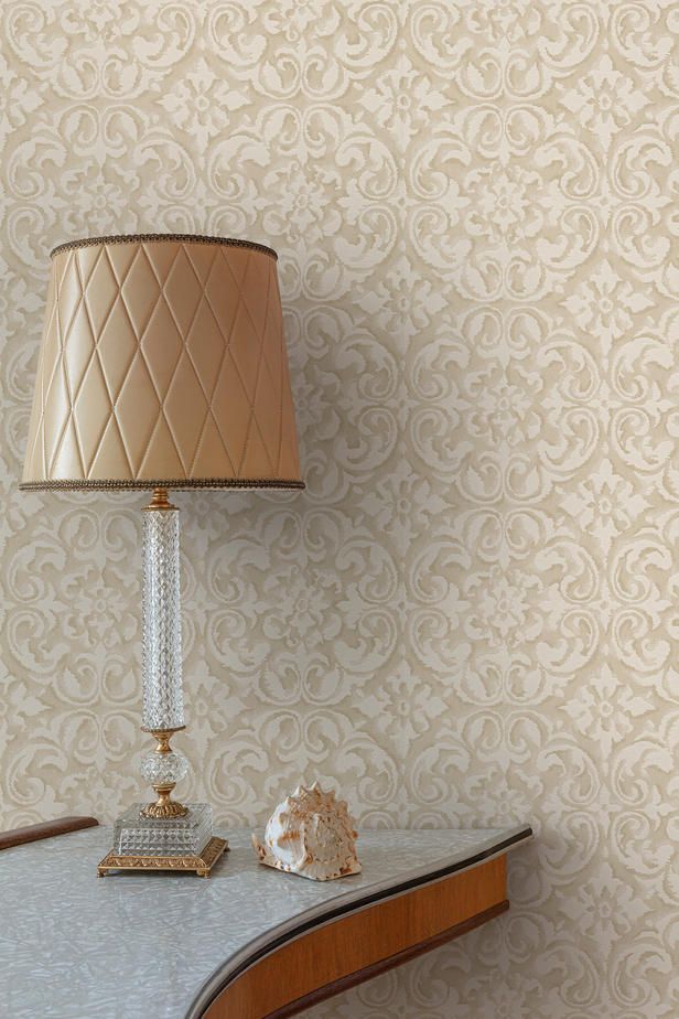 a lamp sitting on top of a wooden table next to a wallpapered wall