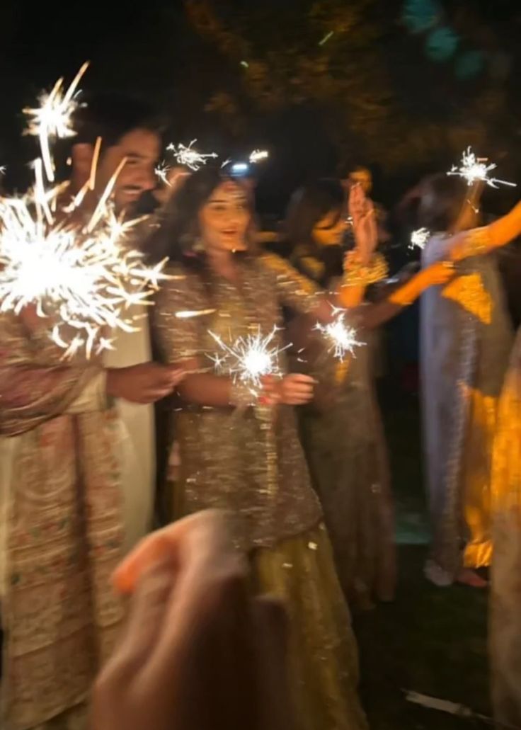 two people holding sparklers in their hands at night time with other people standing around