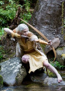 an image of a woman holding a bow and arrow in the water while sitting on some rocks