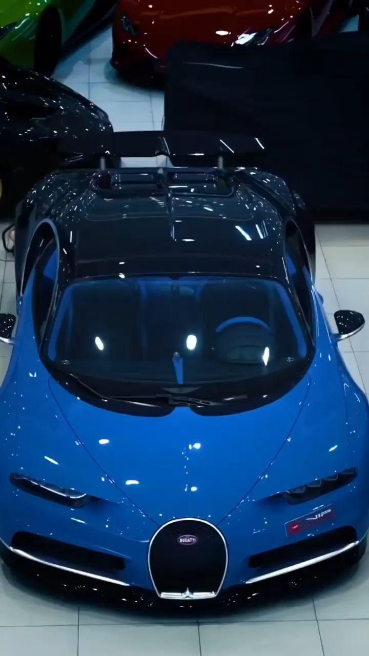 a blue bugatti is parked in a showroom with other cars behind it