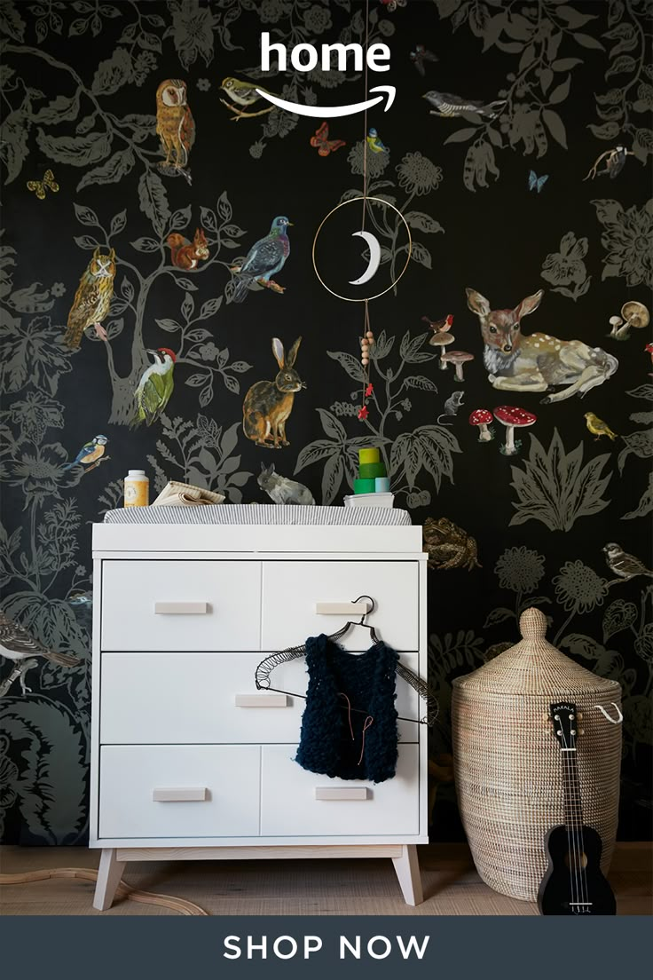 a white dresser sitting next to a black wall with birds on it and a guitar