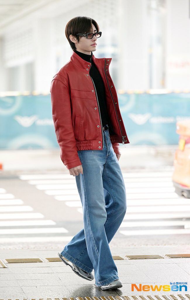 a young man wearing glasses and a red jacket is standing in an airport with his hands in his pockets