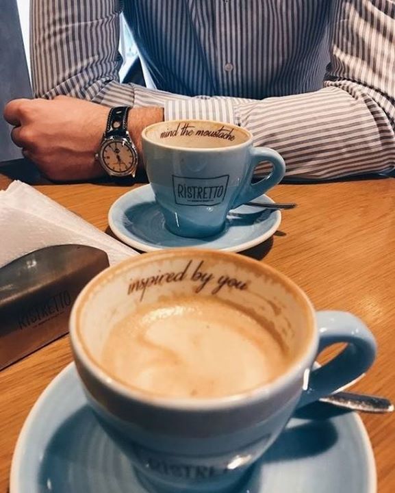 two cups of coffee sitting on top of blue saucers next to each other with writing on them