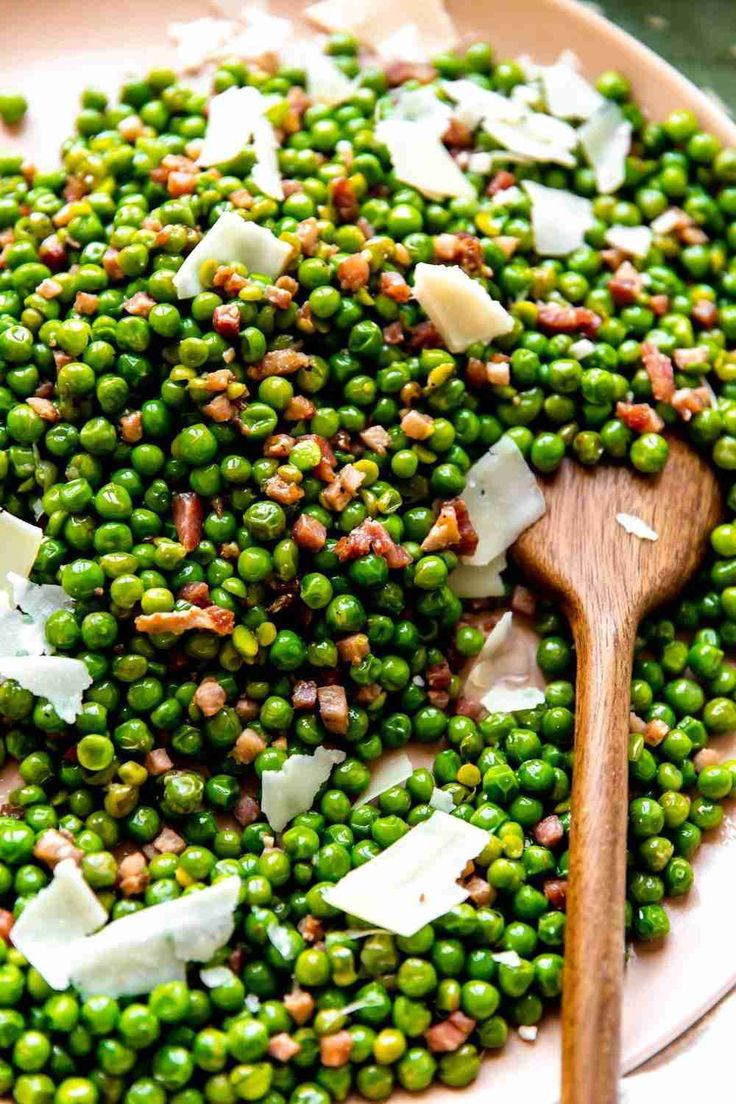 a plate with peas and parmesan cheese on it next to a wooden spoon