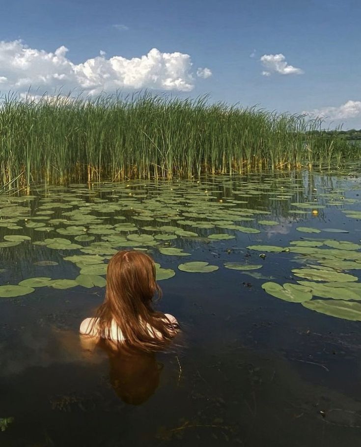 a woman is floating in the water surrounded by lily pads and tall green reeds