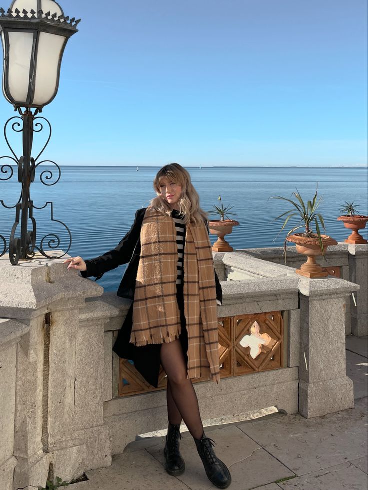 a woman standing next to a light pole near the ocean