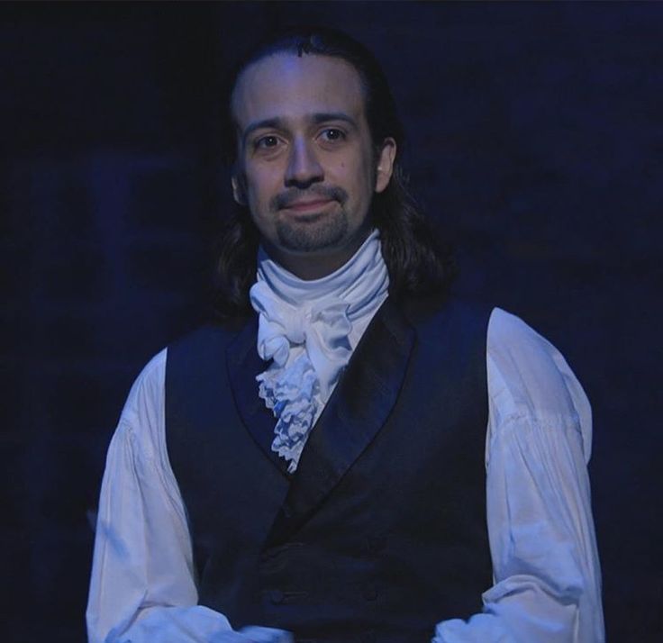 a man with long hair wearing a vest and white gloves