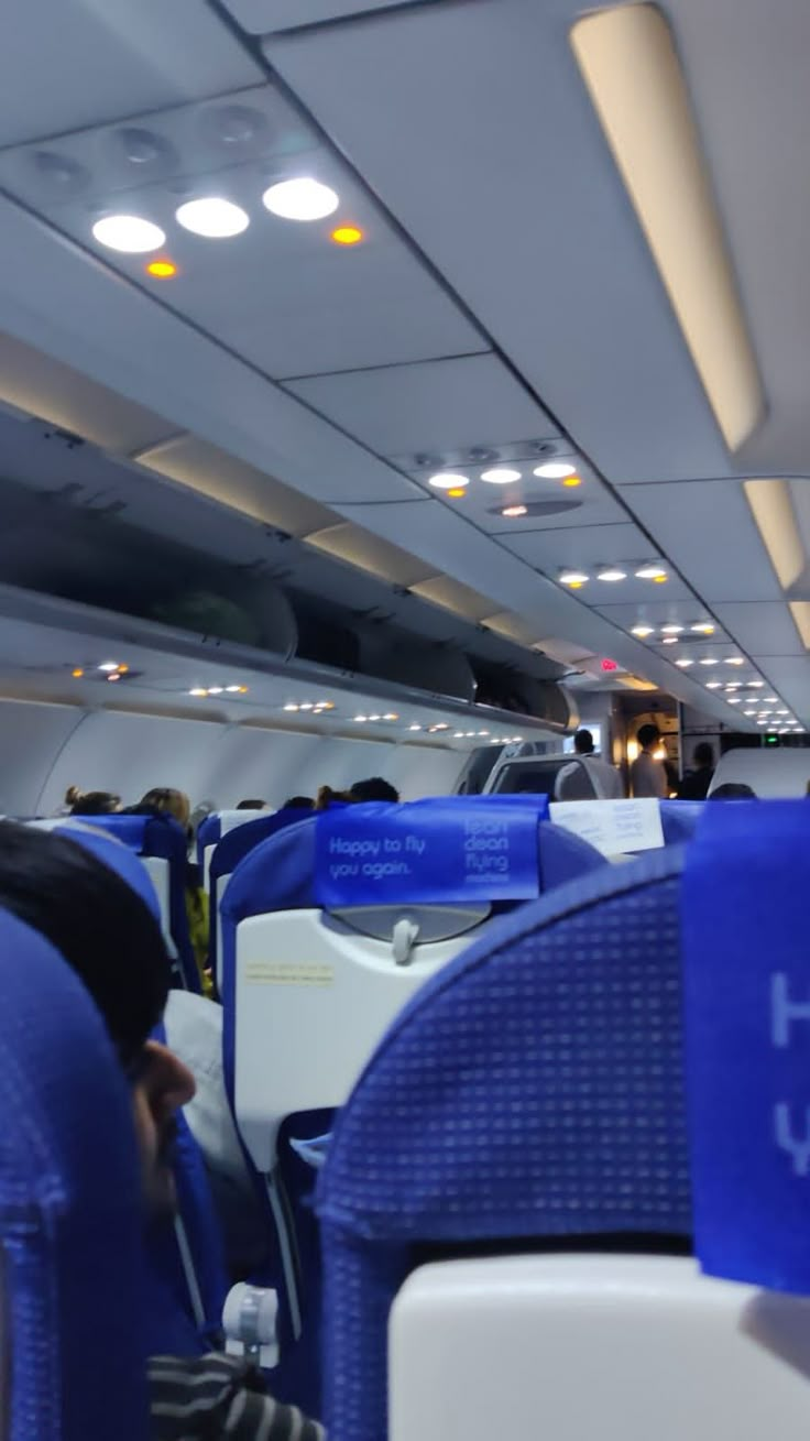 the interior of an airplane with blue seats and white walls, while people are seated on either side