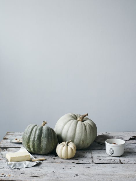 three white pumpkins, one green and one orange on an old wooden table with a cup