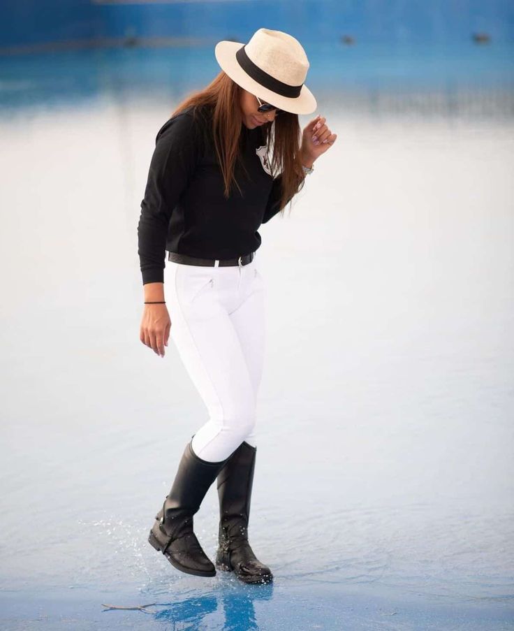 a woman in white pants and black shirt is standing on the ice with her hat over her head