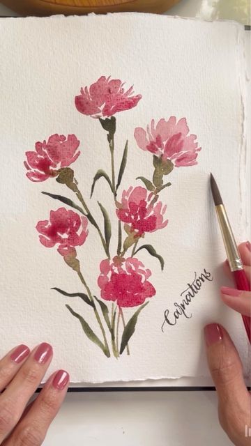 two hands are holding a pen and drawing flowers on a piece of paper with watercolor pencils