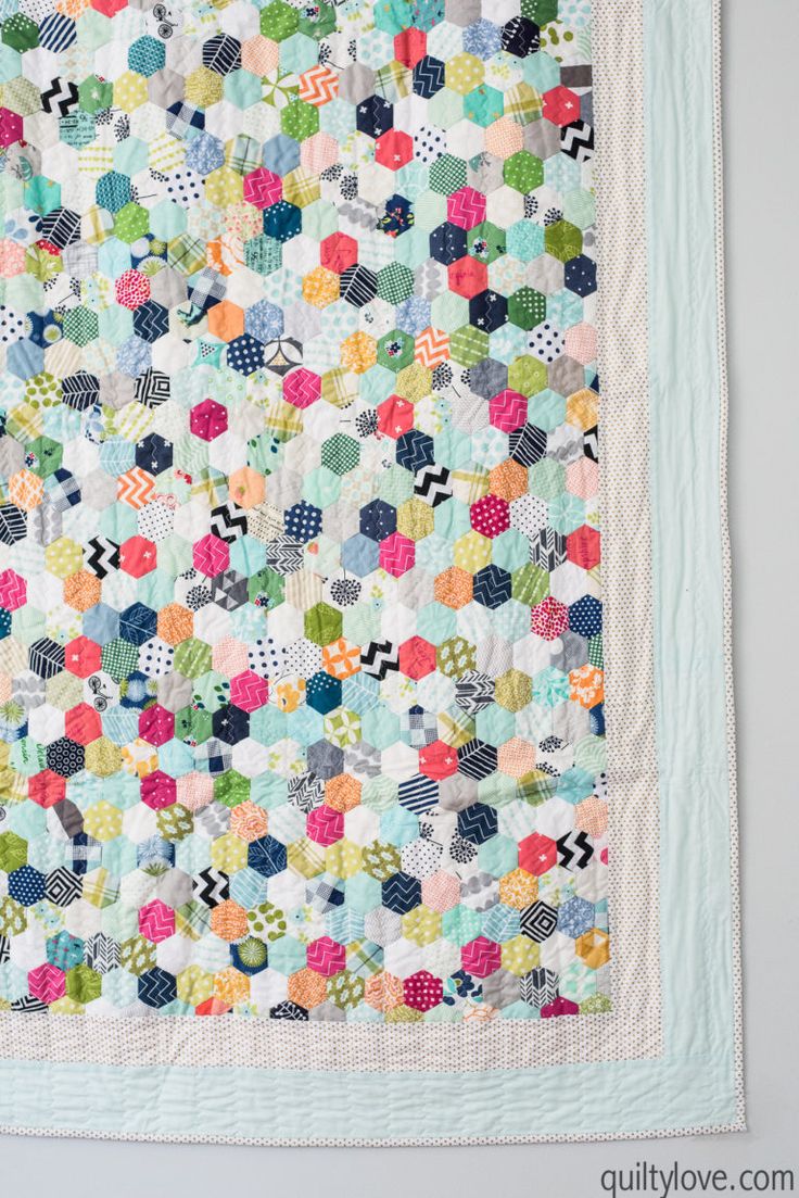 a colorful quilt hanging on the wall in front of a white wall with a light blue border