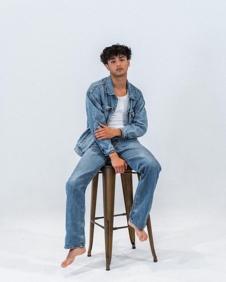 a man sitting on top of a metal stool with his arms crossed and legs crossed