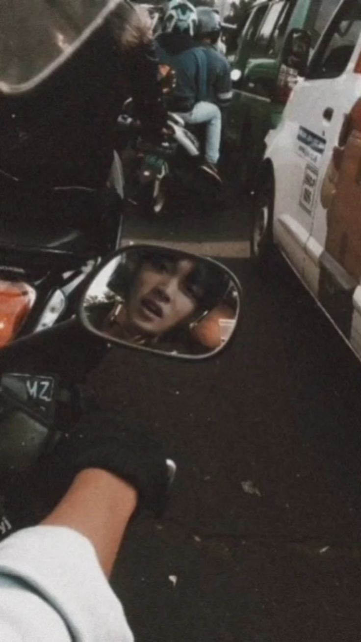 a person's reflection in the side view mirror of a motorbike parked next to other vehicles