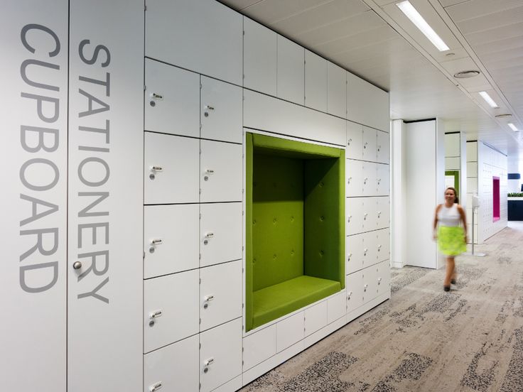 a woman walks past lockers in an office building with white walls and green doors