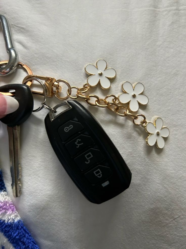 a hand holding a car key chain with flowers on it and a pair of keys in the other hand