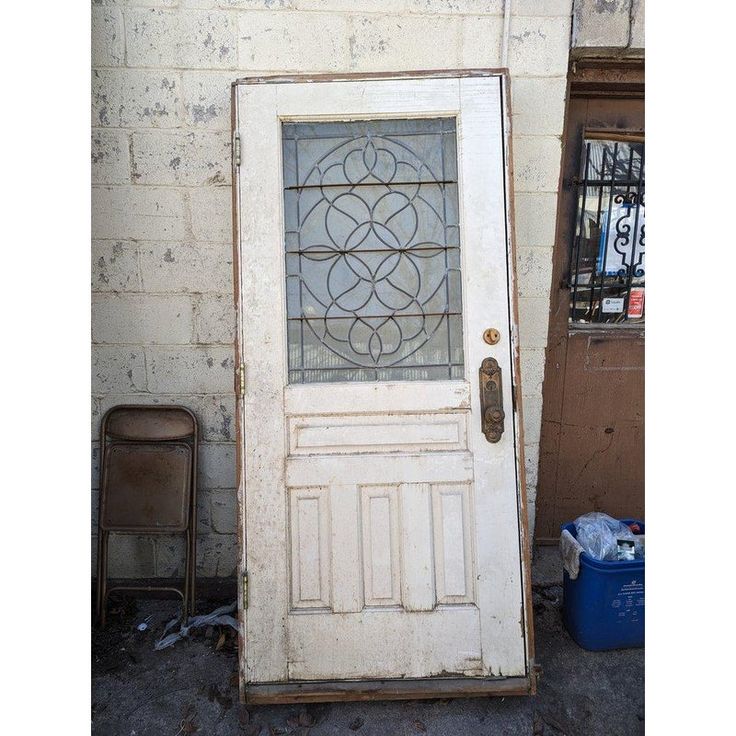 an old white door with stained glass on it and a trash can in the background