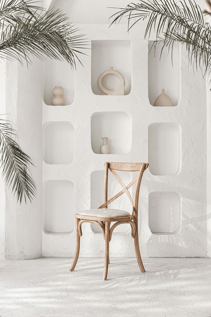 a wooden chair sitting in front of a white wall with shelves on it and palm leaves