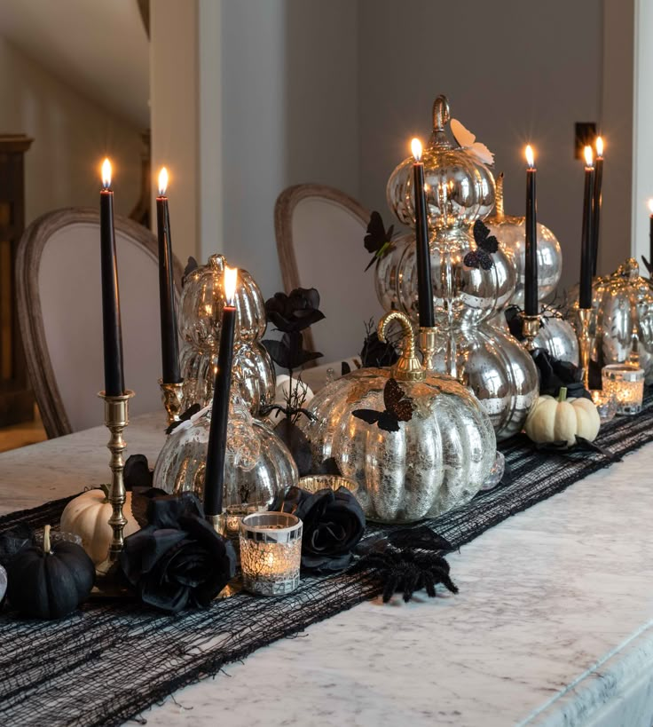 a table topped with lots of silver pumpkins and black candles on top of it